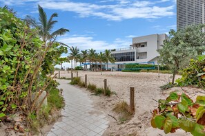 Un sendero conduce a un edificio moderno de techo plano y amplias ventanas, rodeado de vegetación y palmeras.