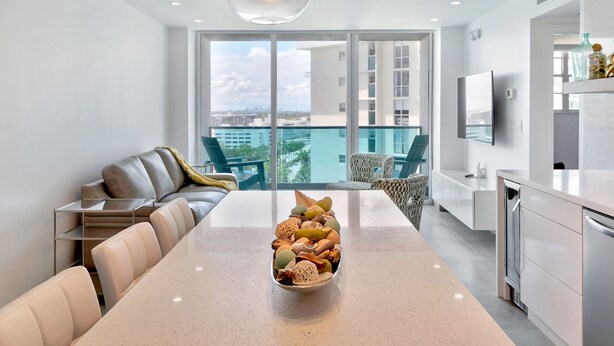 A modern kitchen with a central island, a dining area with a long table, and a balcony with a city view. - Beach front 2/1.5 luxuriously renovated space NEW! Rare find ... (Hollywood)