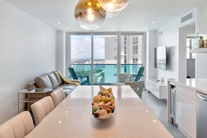 Una cocina moderna con una isla central, un comedor con una mesa larga y un balcón con vistas a la ciudad.