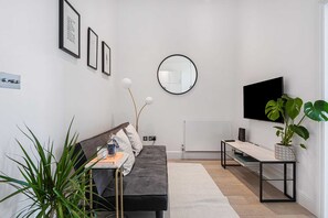 A modern living room with a sofa, a coffee table, a TV, and a potted plant.