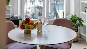 Ein runder Tisch mit Marmorplatte, umringt von rosafarbenen Stühlen, einer Obstschale, einer Flasche und zwei Weingläsern.