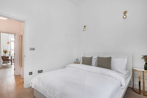A bedroom with a large bed, bedside tables, a nightstand, and a wall-mounted light fixture. - Lady on the Lane, 2 bed Primrose Hill - by Out of Office Lifestyle (London)