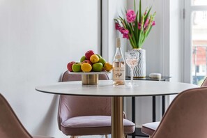 A round table with a fruit bowl, a bottle, and a glass. Pink chairs surround the table. - Lady on the Lane, 2 bed Primrose Hill - by Out of Office Lifestyle (London)