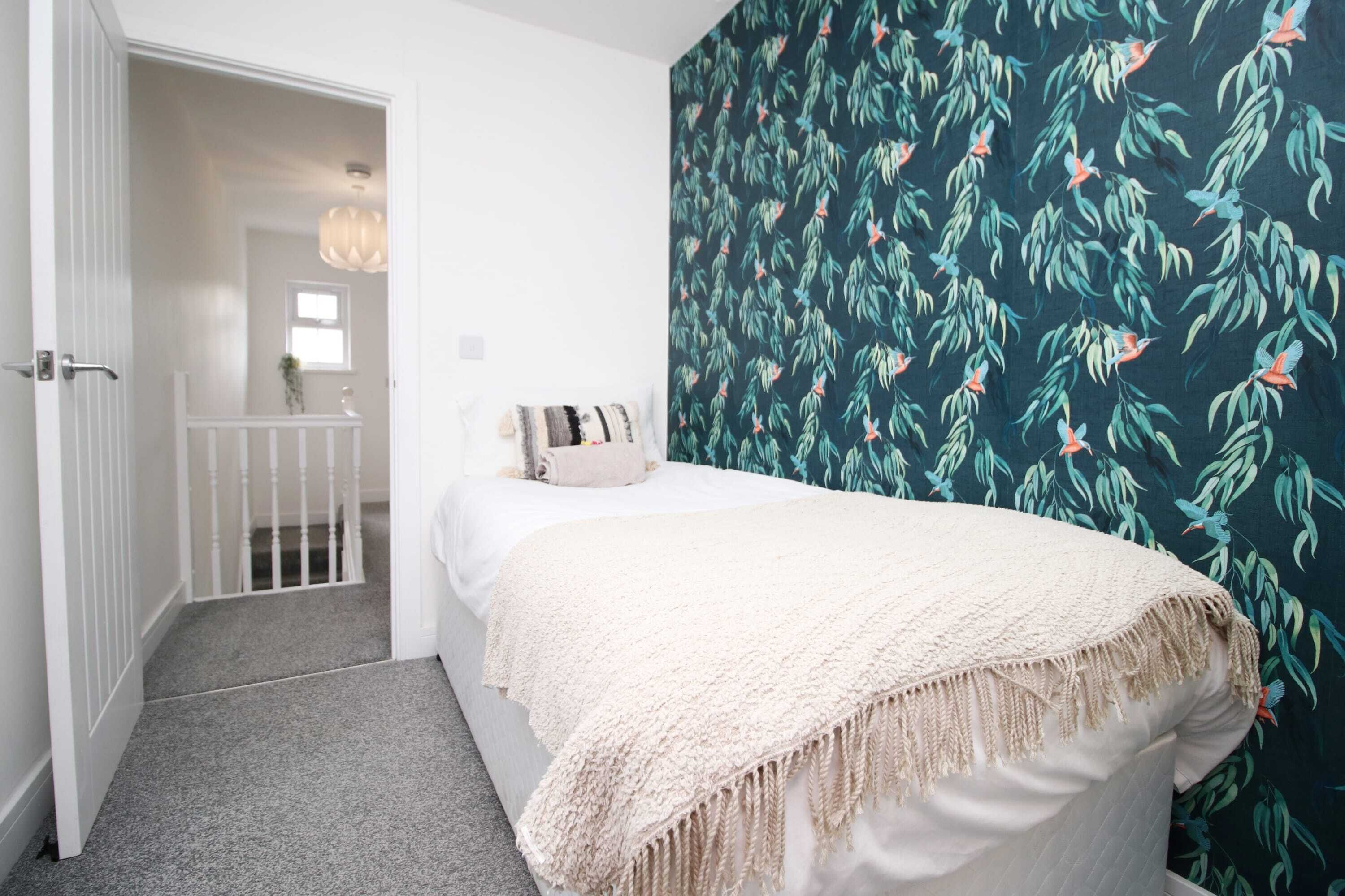 A bedroom with a bed, a white door, and a wall with a leafy pattern.