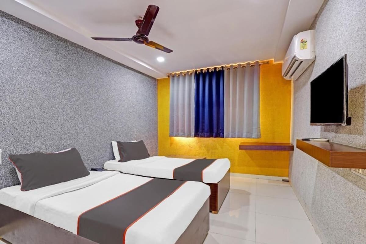Habitación de hotel con dos camas, ventilador de techo, aire acondicionado, televisor y ventana con cortinas.