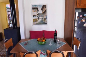 Un comedor con una mesa dispuesta para dos personas, un cuenco de fruta, una botella de vino y un cuadro en la pared.