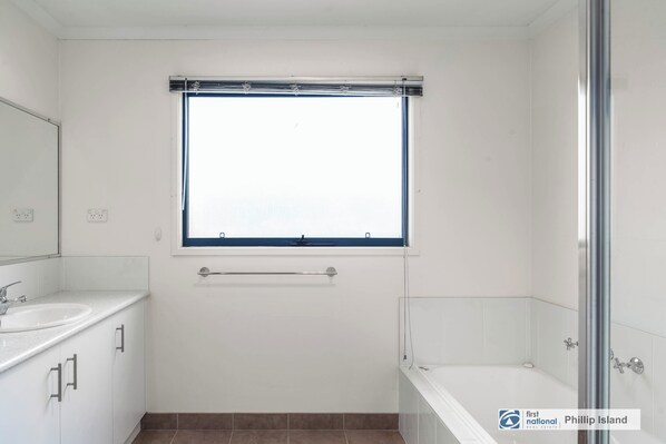 A bathroom with a white sink, a mirror, a window, and a bathtub.