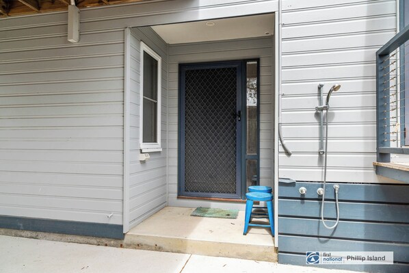 A house with a screened door, a small blue stool, and a metal shower enclosure.