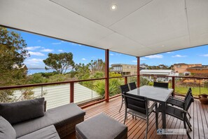 A covered outdoor area with a table and chairs, a sofa, and a view of the sea and surrounding buildings. - Water views150m from safe beach, 2 STORY holiday house in Ventnor free WIFI (Ventnor)