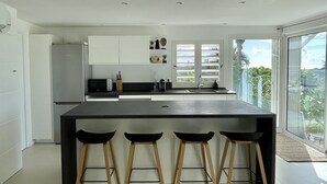 A modern kitchen with a large island, bar stools, white cabinets, and a view of the outdoors.