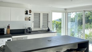 A modern kitchen with a large island, bar stools, and a view of greenery outside.