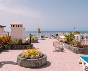En takterrass med pool, solstolar och utsikt över havet.