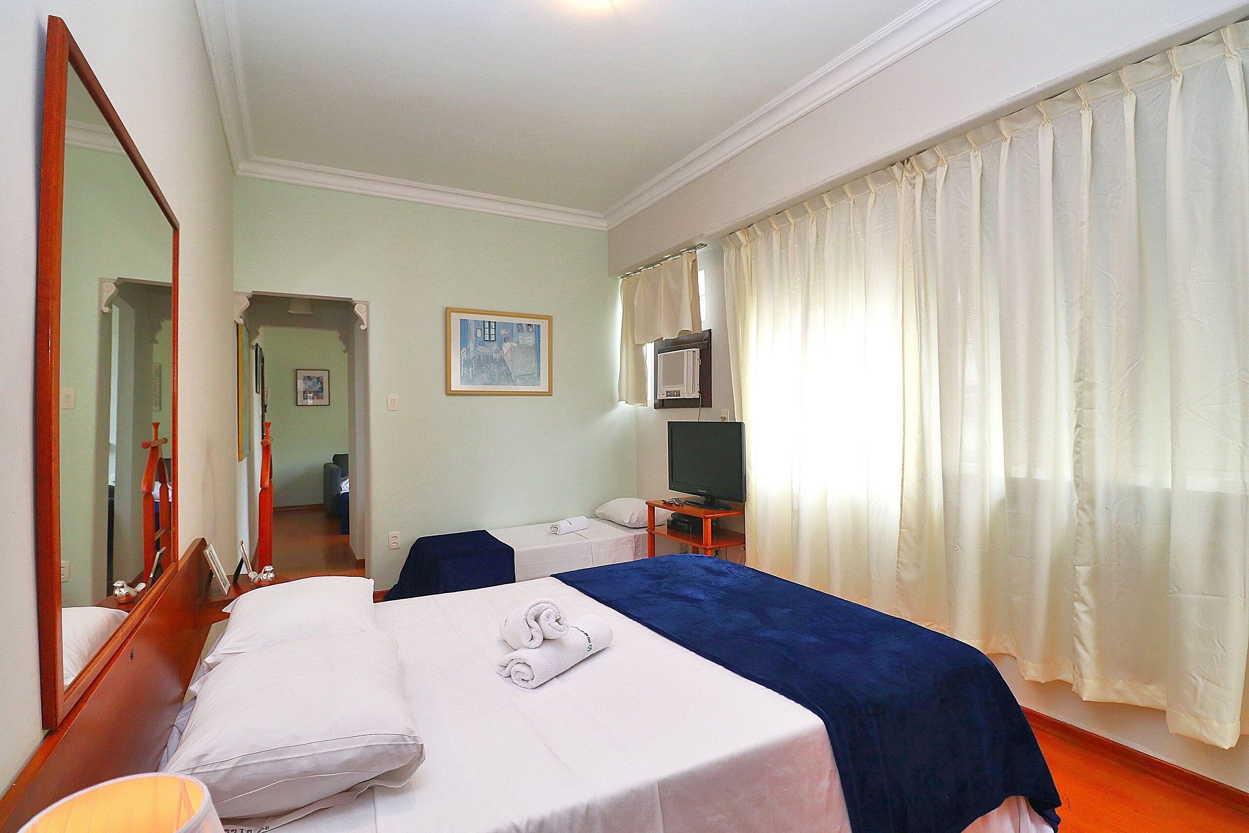 A hotel room with two beds, a television, a mirror, and a window with curtains.