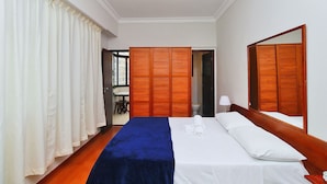 A hotel room with a bed, a wooden wardrobe, a mirror, and a bathroom visible through an open door.
