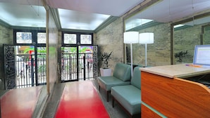 A reception area with a desk, two green sofas, a red carpet, and a view through a glass door to the outside.
