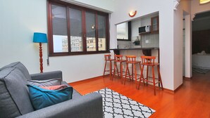 A compact living space with a grey sofa, a patterned rug, and a kitchen area with a microwave and bar stools.