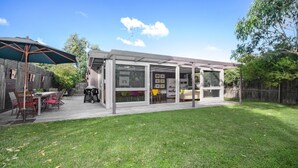 Ein überdachter Patio-Bereich mit Grill, Sitzgelegenheit im Freien und Blick auf den Garten.
