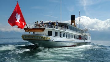 A boat with a white hull and a red flag, named "LA SUISSE," sailing on the water.