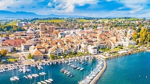 An aerial view of a coastal town with a marina filled with boats, historic buildings, and a clear blue sky. - Afterwork Hotel (Etoy)