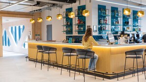 A modern bar area with a wooden counter, black bar stools, and blue shelving with bottles. - Afterwork Hotel (Etoy)