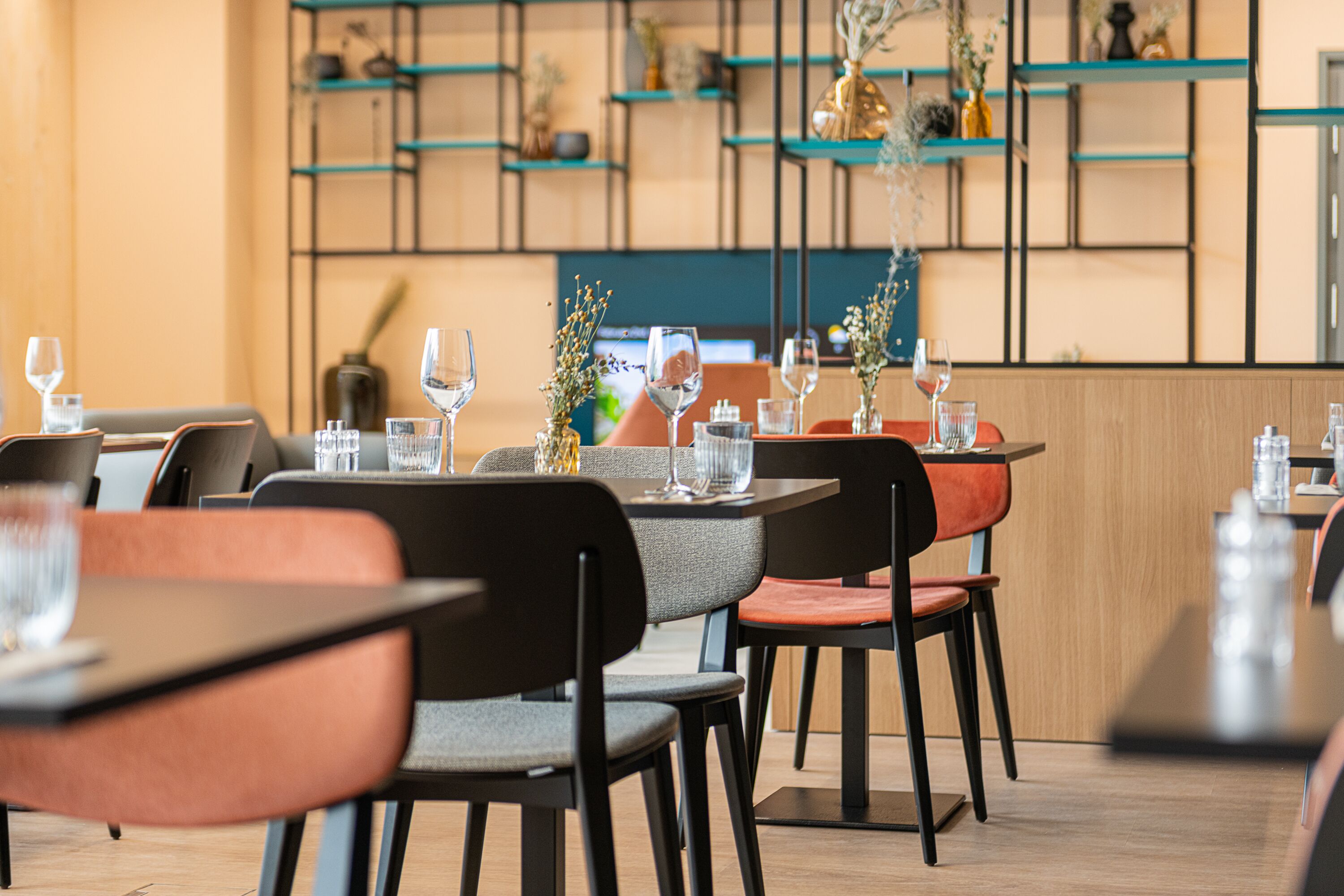 A restaurant interior with tables and chairs, shelves with decorative items, and a wooden accent wall.