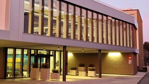 A modern building with large windows and a flat roof, featuring a parking area with potted plants and a sign indicating a parking space. - Afterwork Hotel (Etoy)