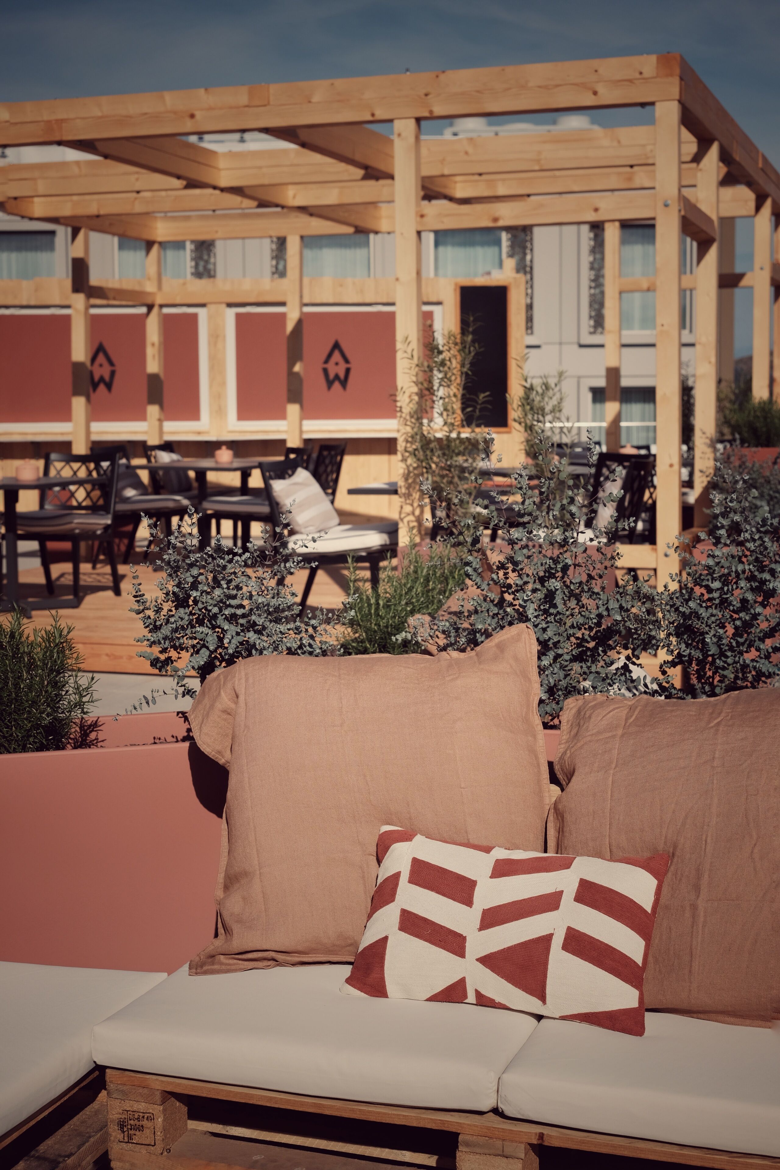 A wooden pergola structure with outdoor seating, including a sofa and chairs, surrounded by potted plants.