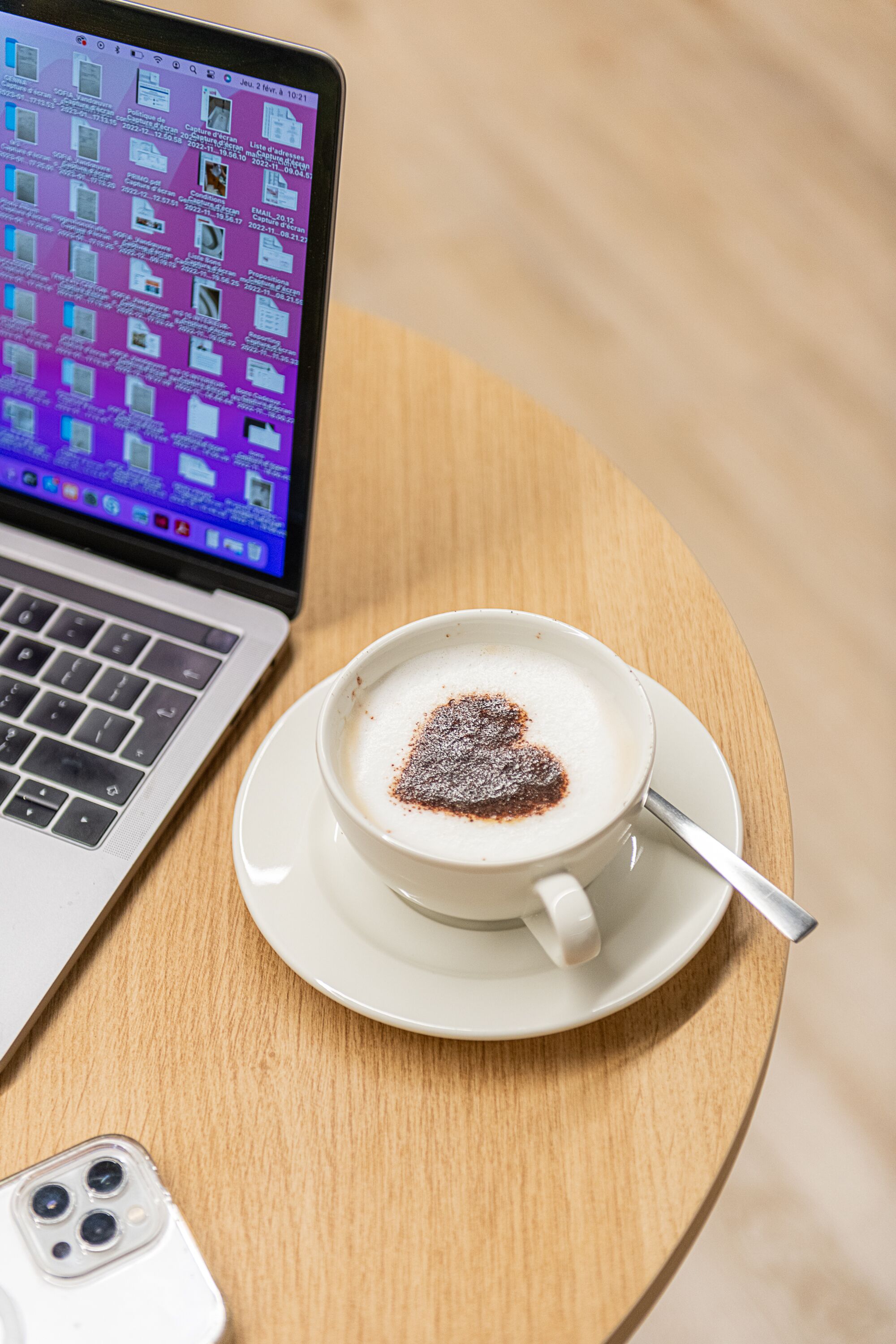 A laptop on a wooden table with a cup of coffee and a smartphone.