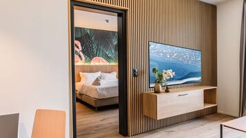 Una habitación de hotel moderna con pared de paneles de madera, un televisor de pantalla plana grande, una cama con sábanas blancas y piso de madera.