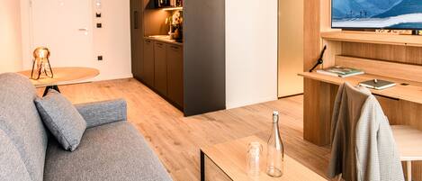 Ein modernes Wohnzimmer mit einem grauen Sofa, einem Holztisch und einem Fernseher, der eine verschneite Landschaft zeigt.