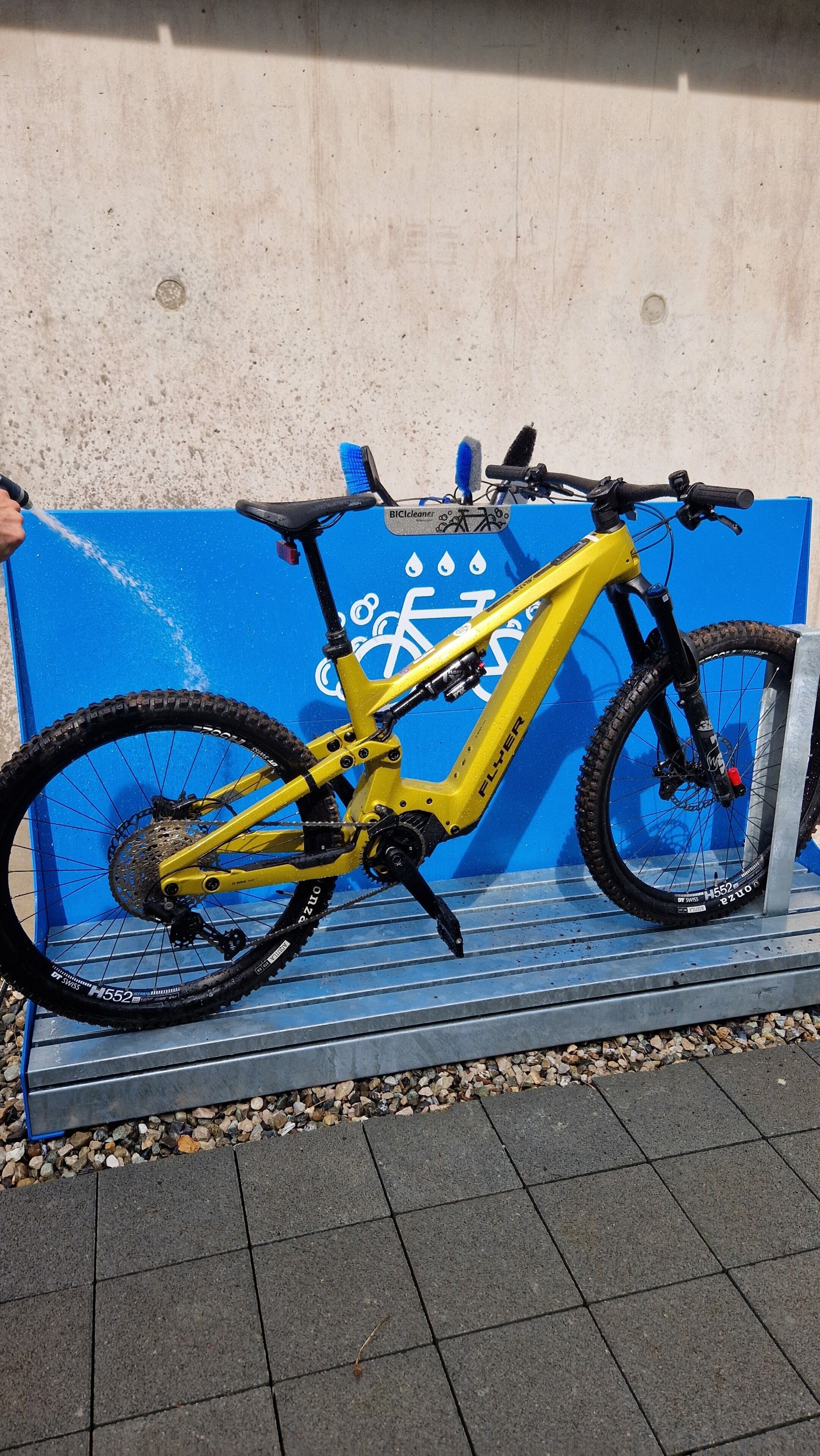 Una bicicleta de montaña amarilla estacionada sobre un banco azul, con un muro de concreto al fondo.