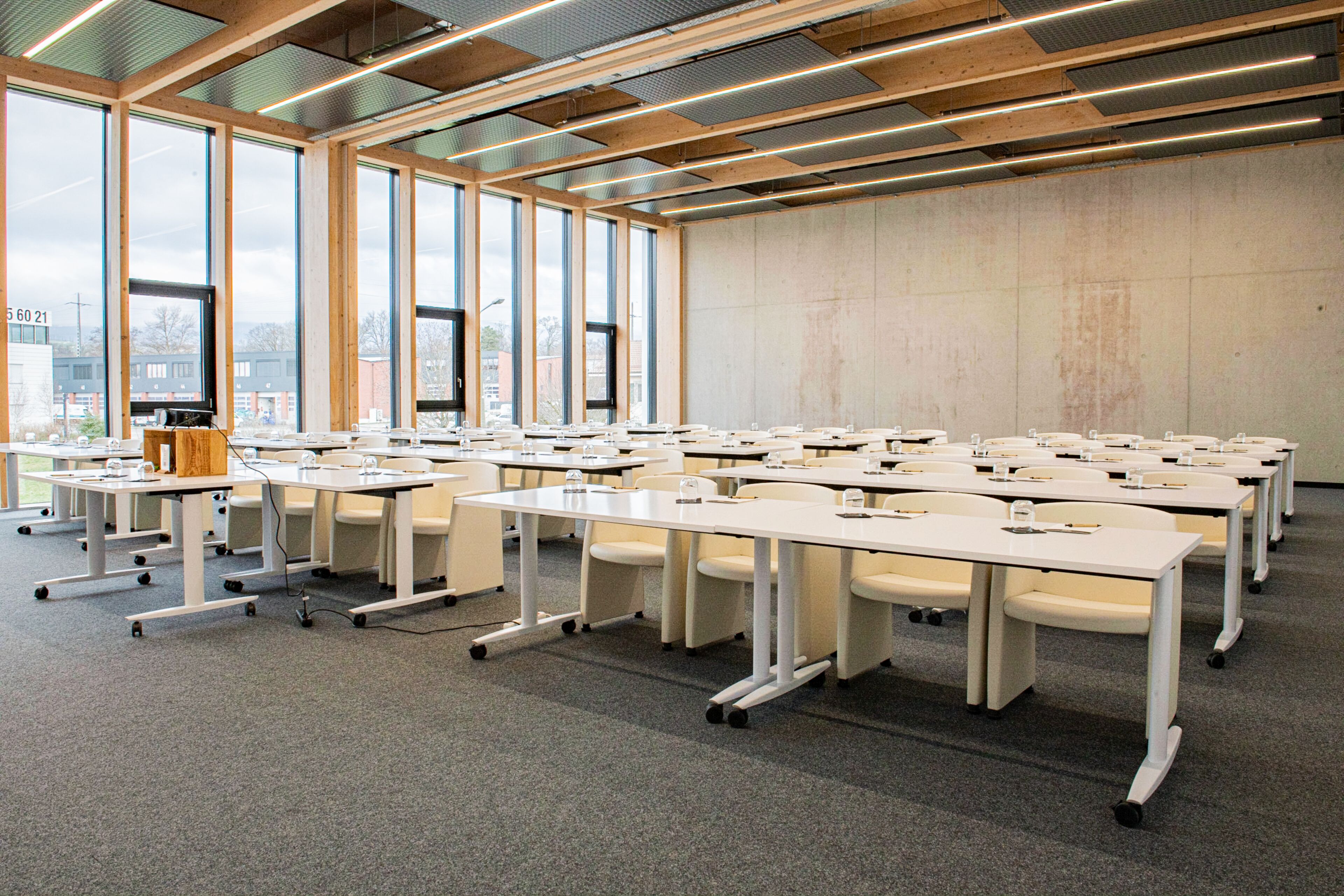 A conference room with multiple tables and chairs, large windows, and a high ceiling with exposed beams.