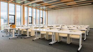 A conference room with multiple tables and chairs, large windows, and a high ceiling with exposed beams.