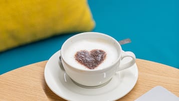 A cup of coffee with a heart-shaped design on the foam, placed on a saucer on a wooden table.