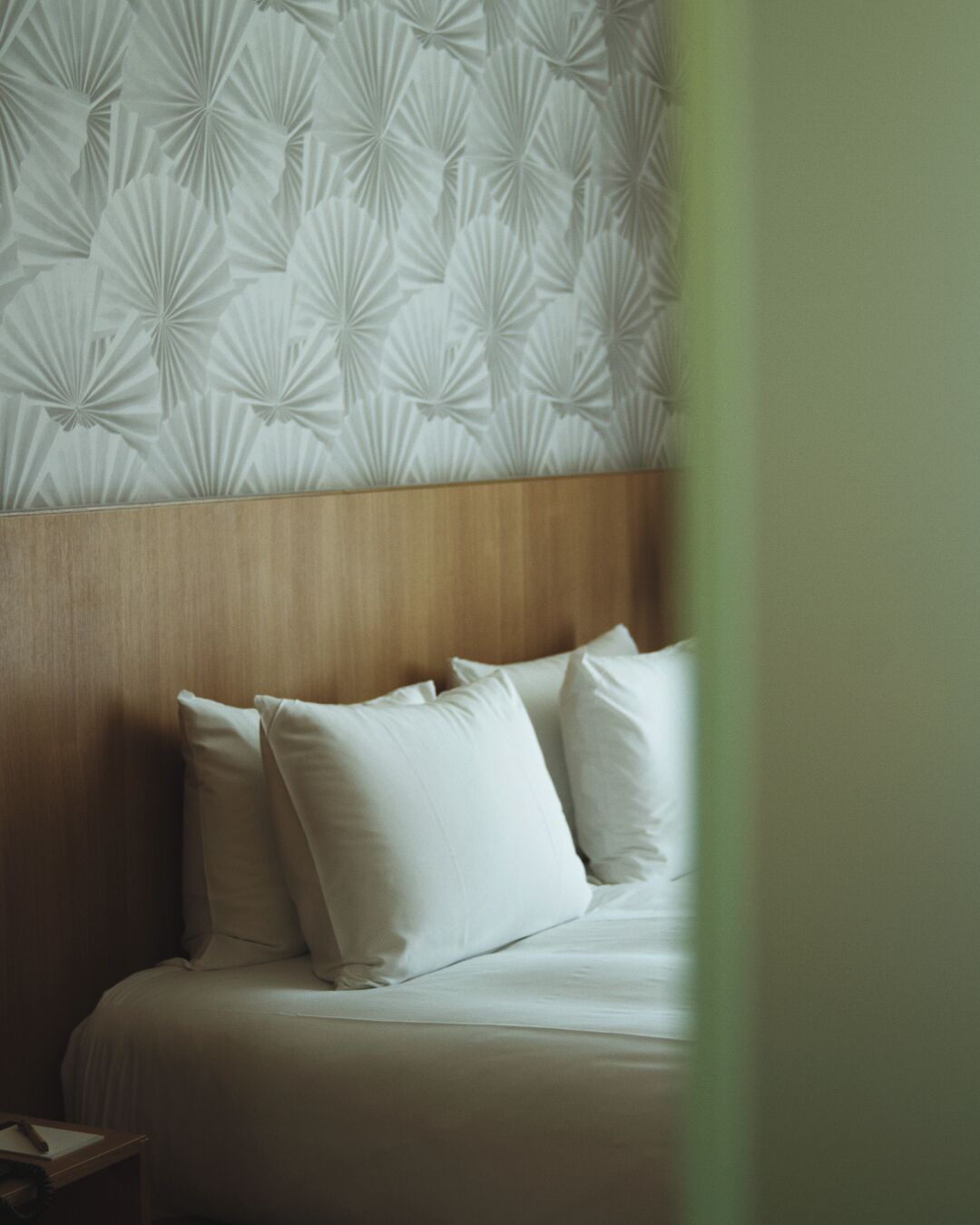 Un lit bien fait, avec une literie et des oreillers blancs, une tête de lit en bois et un mur orné d’un motif.