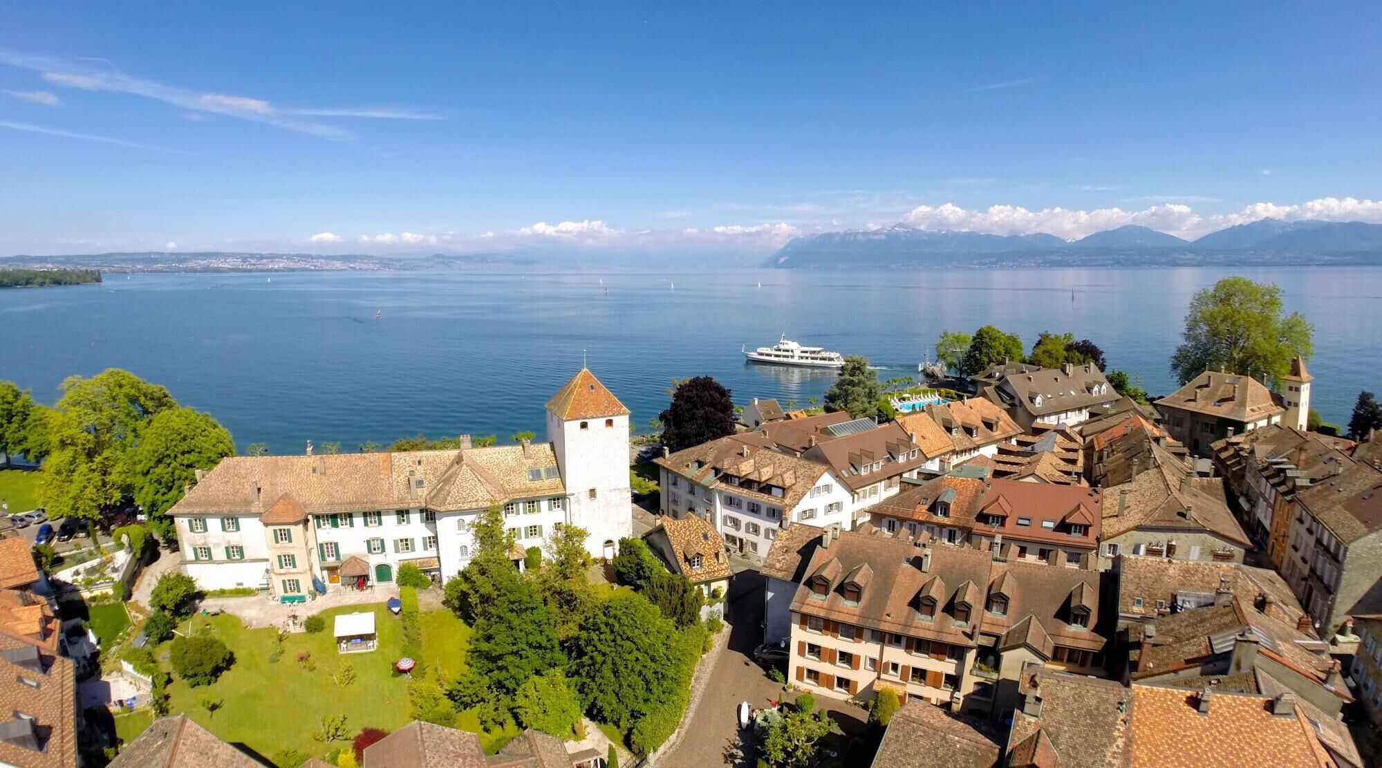 A lakeside town with historic buildings, a prominent tower, and a boat on the water.