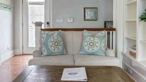 Een woonkamer met een beige bank, gestreepte kussens, een houten salontafel en een lijst met een foto aan de muur.