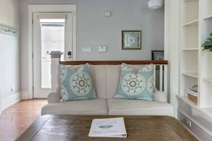 A living room with a beige sofa, patterned cushions, a wooden coffee table, and a framed picture on the wall.