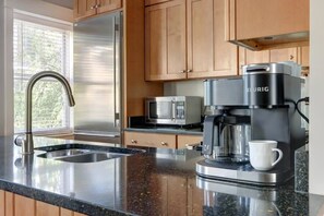 A modern kitchen with a stainless steel refrigerator, a coffee maker, a microwave, and a sink with a faucet.