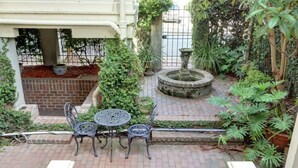 Een binnentuin met een terras van bakstenen, een fontein en planten in potten.