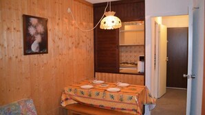 A wooden room with a dining table set for four, a hanging light fixture, and a door leading to another room. - 10m from ski slopes, 5th floor, view mountain, balcony, tv, ski locker, 28m², Les Menuires (Les Menuires)
