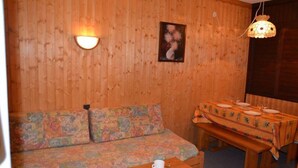 A wooden cabin interior with a sofa, a dining table set for two, and a wall-mounted light fixture. - 10m from ski slopes, 5th floor, view mountain, balcony, tv, ski locker, 28m², Les Menuires (Les Menuires)