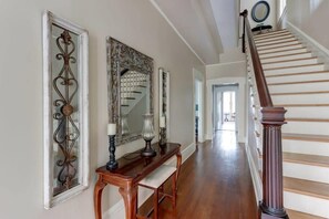 Un pasillo con una escalera de madera, un espejo decorativo y una consola con lámpara.