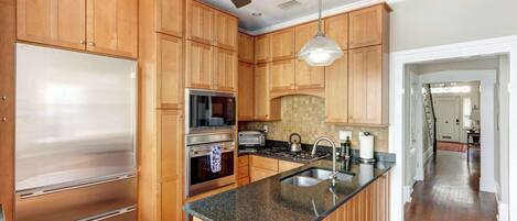 Una cocina con armarios de madera, un refrigerador de acero inoxidable, un horno, un microondas, una estufa y un ventilador de techo.