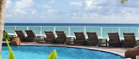 Ein Poolbereich mit Liegestühlen und Blick auf das Meer.