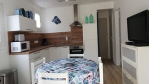 A compact kitchen with a microwave, stove, and sink. There is a bed with a patterned bedspread and a television on a stand.
