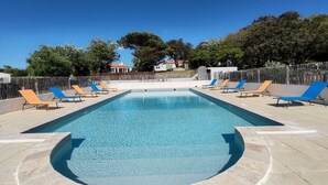 A rectangular swimming pool with a clear blue water surface, surrounded by a tiled deck. There are multiple lounge chairs with blue and orange cushions arranged around the pool.