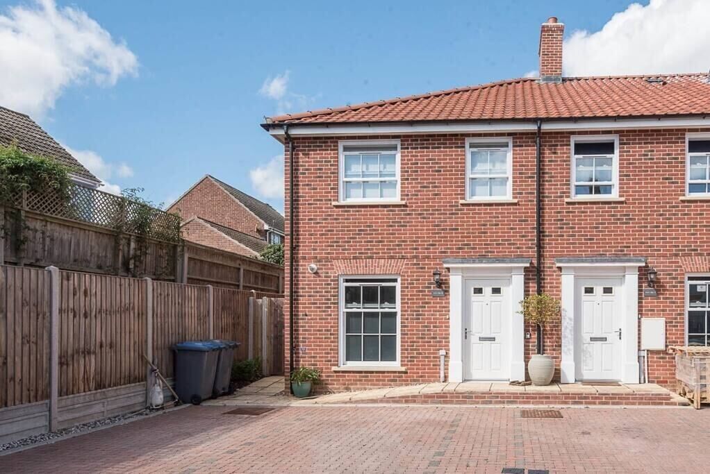 A two-story brick house with a red-tiled roof, white doors, and a brick driveway.