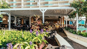Vestíbulo de hotel con un área de estar al aire libre techada, diversas plantas y un letrero que dice 'Cinnamon's'.