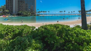 Una playa con agua turquesa cristalina, palmeras y un alto edificio de hotel al fondo.